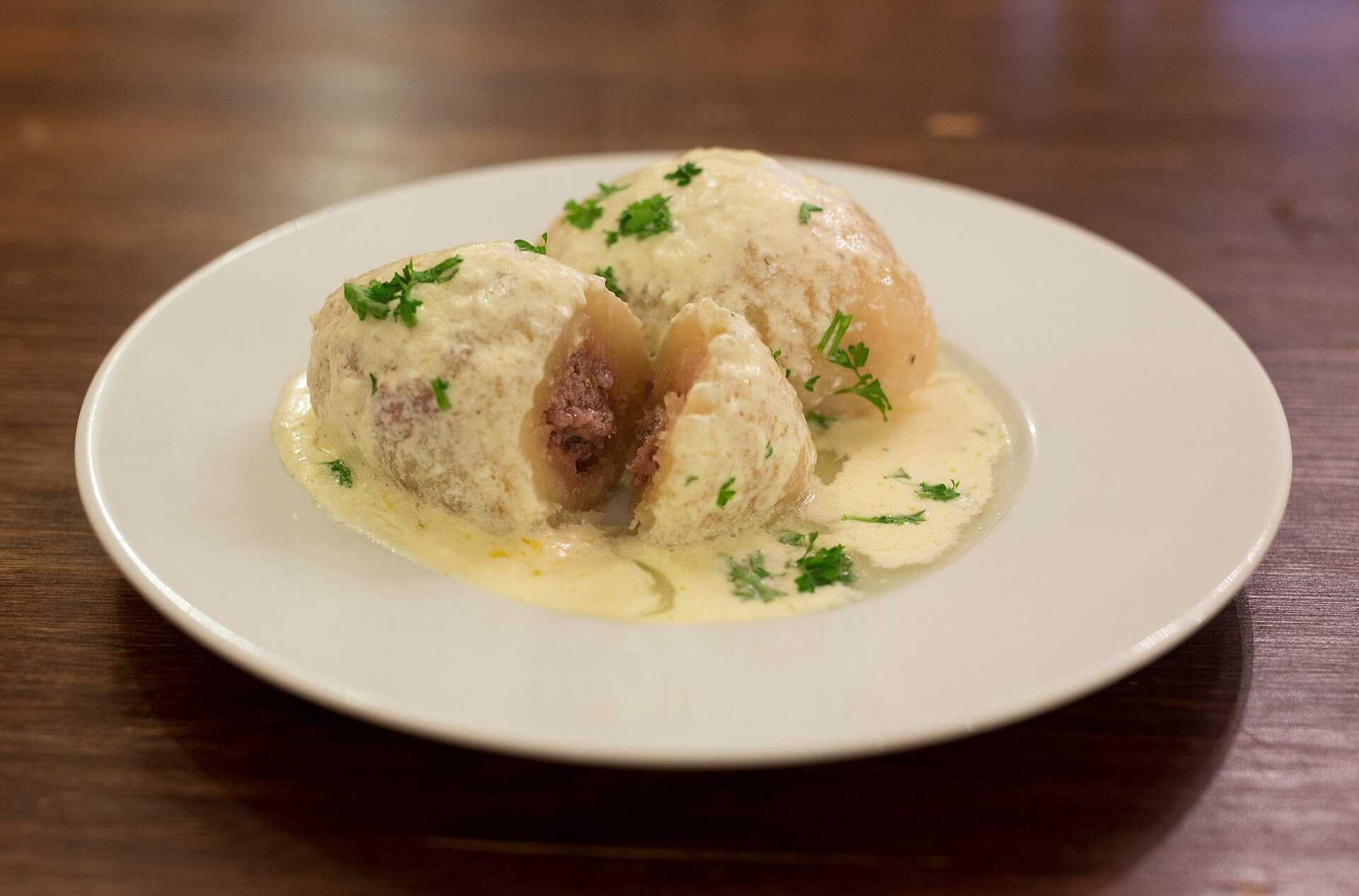 Two large oval potato dumplings topped with sour cream and bacon