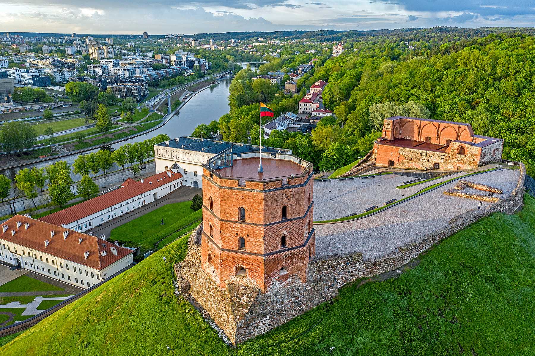 Red brick tower on a green hill with the Lithuanian flag on top